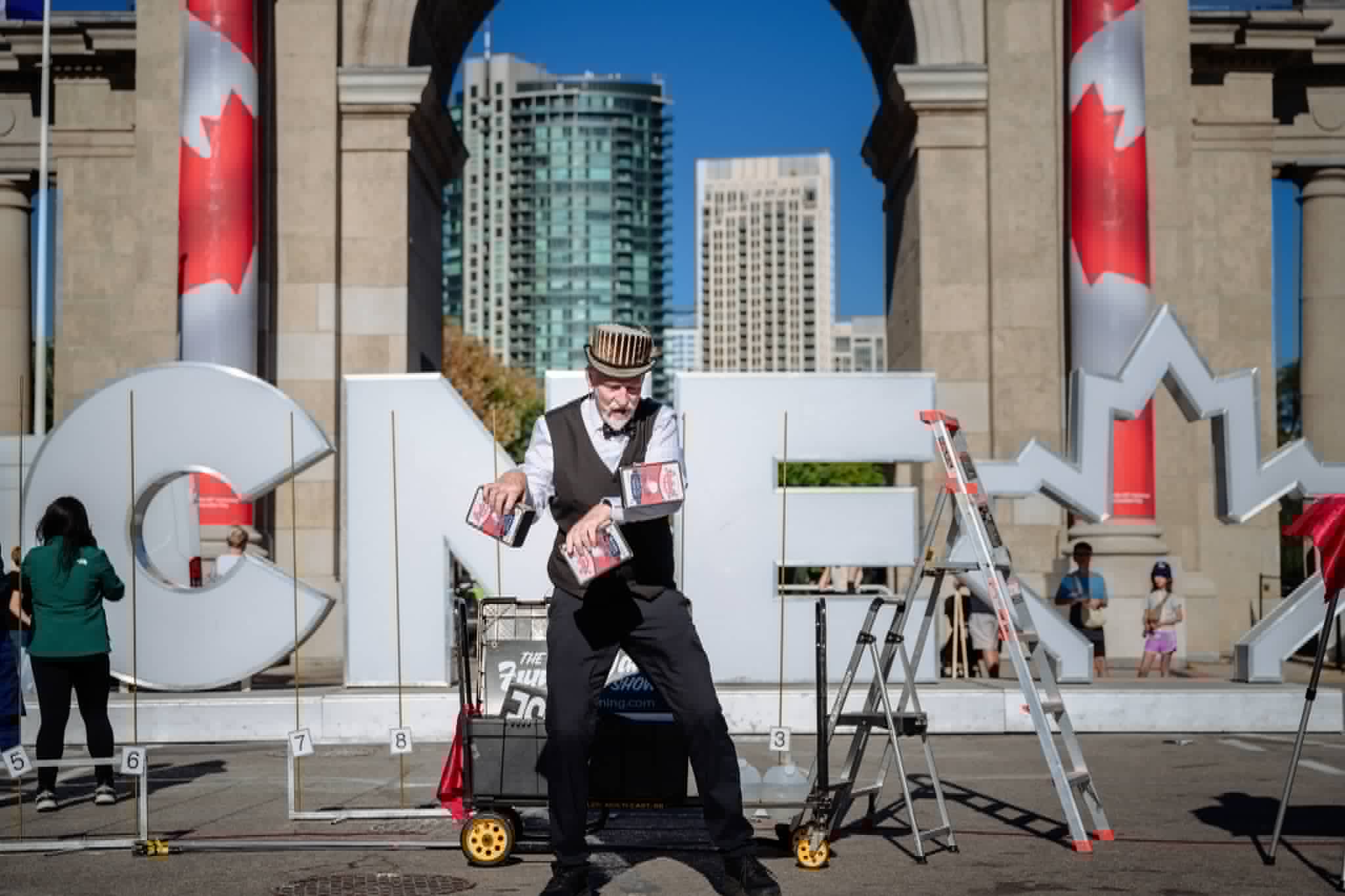 Cigar box juggling manipulation in front of the CNE sign in Toronto