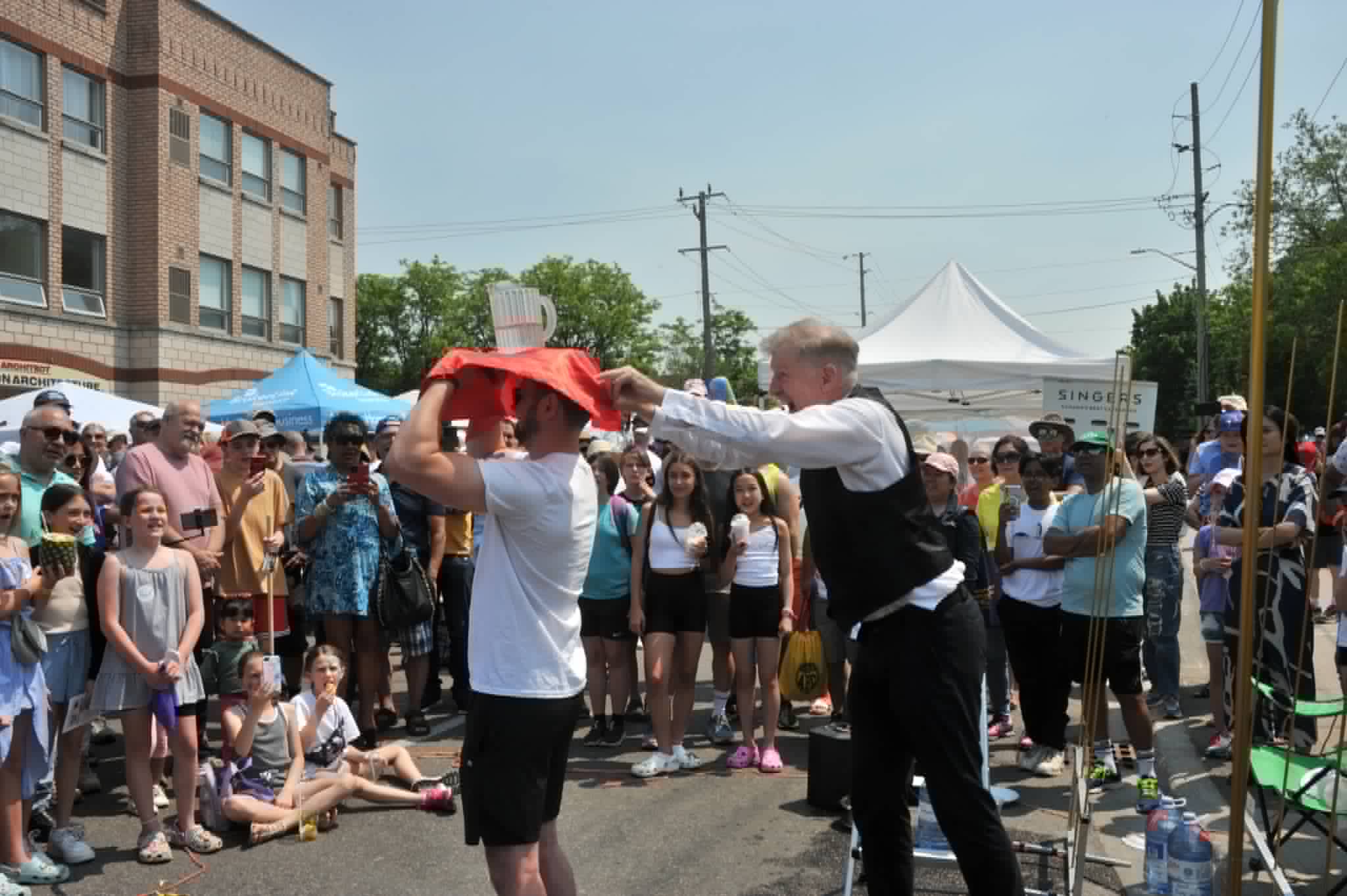 Comedy tablecloth pull over an audience volunteer's head at a summer street festival
