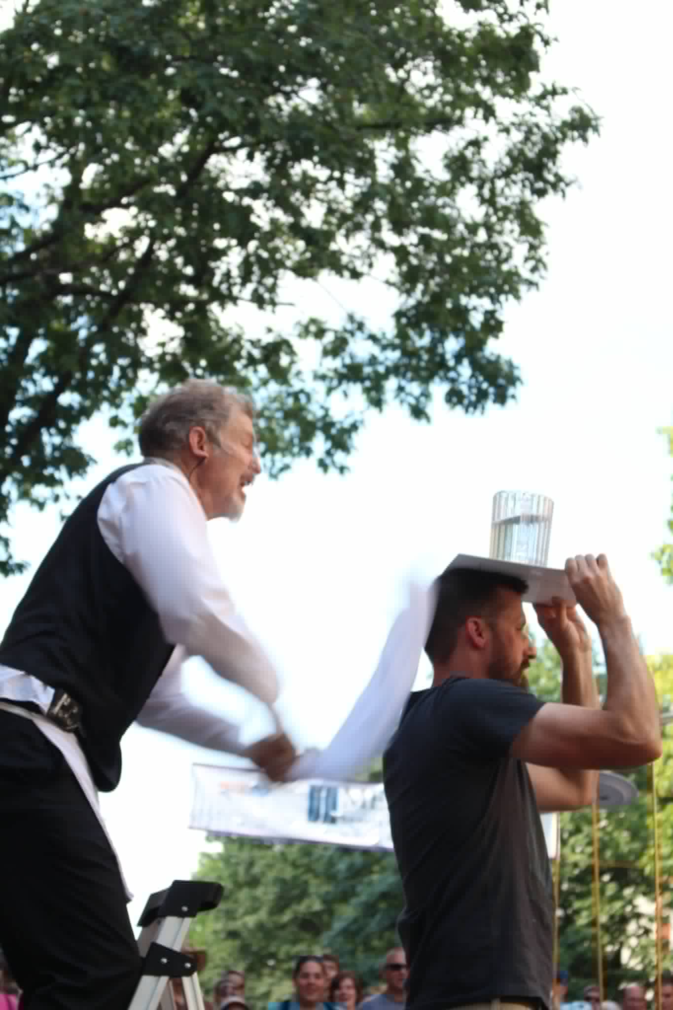 Pulling a tablecloth from under a full glass of water balanced on a volunteer's head