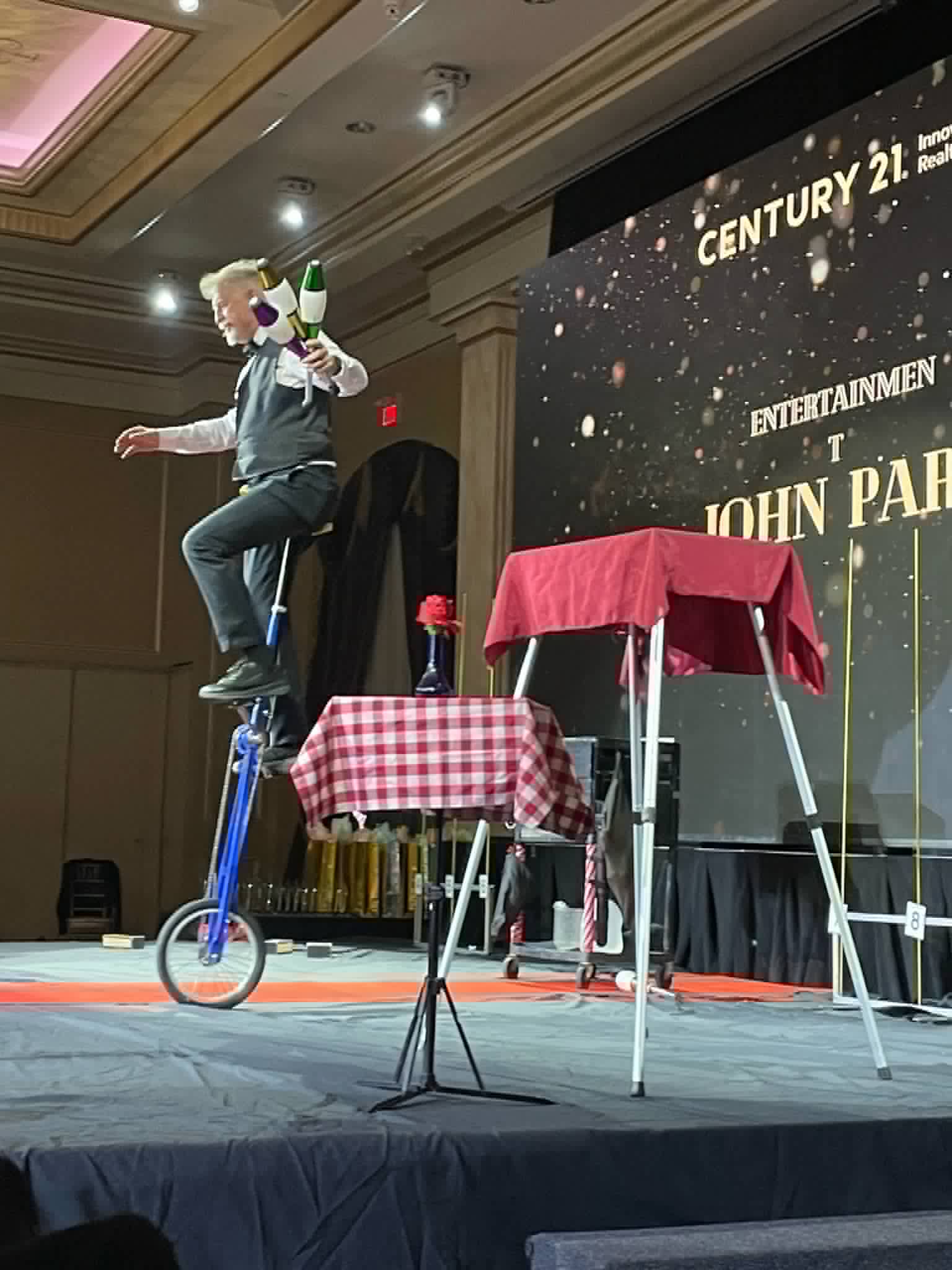 Corporate entertainer John Park juggling pins on a tall unicycle on stage at a corporate awards gala